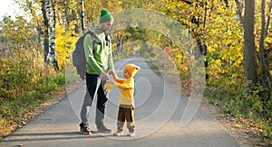 Father and son walking together on empty road in autumn park, enjoying good weather. Beautiful nature in fall season. Parenting