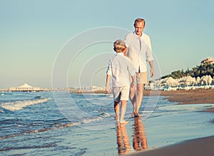 Father with son walking together at the sea surfline