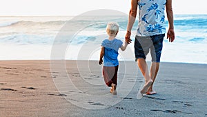 Father and son walks on sunset ocean beach