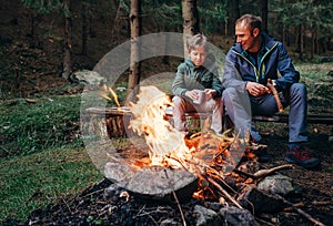 Father with son warm near campfire, drink tea and have conversation photo