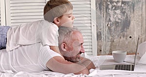 Father and son watch cartoons on a laptop lying on the bed.