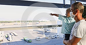 Father and son watching airplanes at the window in the airport waiting for their plane