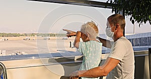 Father and son watching airplanes at the window in the airport waiting for their plane