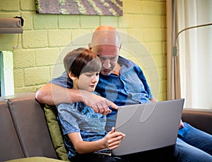 A father and son watching multi media together from laptop. a father teaching a son how to get information from internet network.