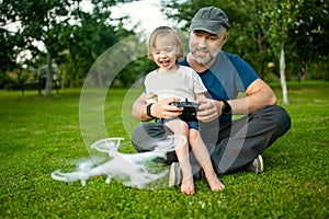 Father and son watching and navigating a drone. Cute toddler boy helping his father to operate a drone by remote control