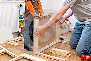 Father and son working on assembling flat-pack furniture for boy`s room.