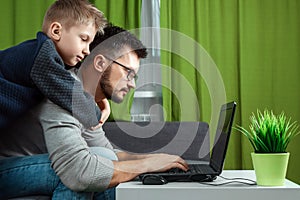 Father and son working on a laptop. Businessman working from home and looking after a child, spending time with a child. The