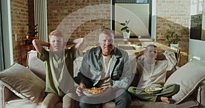 Father and sons eating snacks sitting on the couch