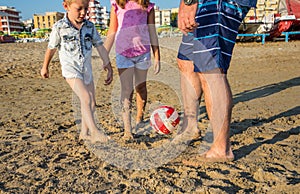 Father and sons playing soccer on the beach