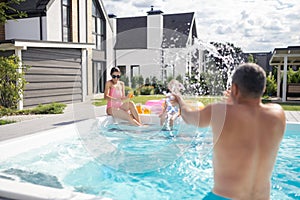 Father splashing water on his daughter and wife in the swimming pool