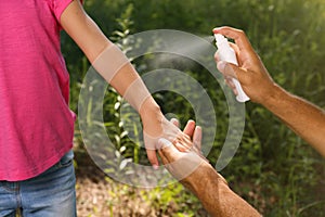 Father spraying tick repellent on his little daughter`s arm during hike in nature, closeup