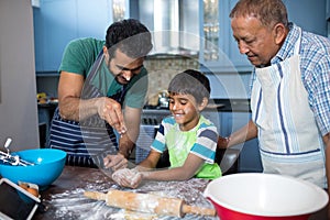 Father sprinkling flour on son hand while preparing food with grandfather