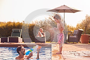 Father Squirting Son With Water Pistol Playing In Swimming Pool On Summer Vacation