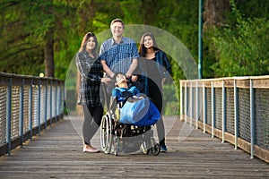 Father standing with biracial children on wooden bridge, special needs photo