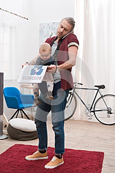 Father standing with son in baby sling holding newspaper and talking