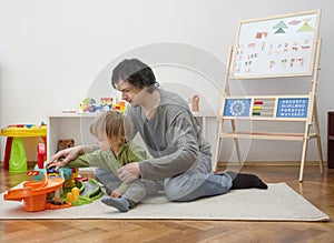 Father and sweet little child boy having fun playing with cars and colorful toys, on the floor, at home. Beautiful family moment,