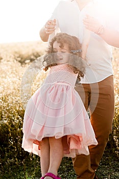 Father swinging a little girl with curly hair in pink dress