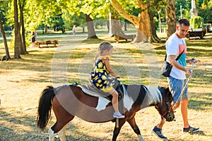 Father take his little dother for a ride on pony horse in park