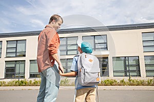 the father takes the boy to school. dad is holding his son\'s hand.