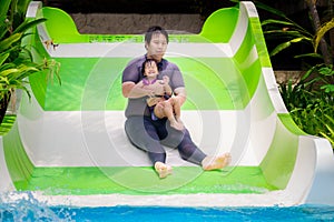 Father takes his daughter to slide into the pool. Family activities. Green and white slides.