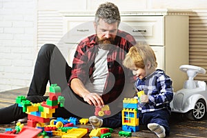 Father takes part in game with son playing on floor holding toy cars. Father and son create toys from bricks. Dad and