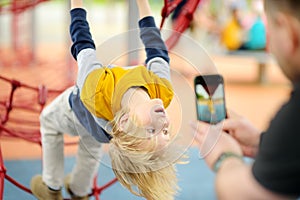 Father is taking a shot of his son having fun during stroll on outdoor playground. Active sport leisure for family with kids.