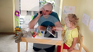 Father talking with mobile phone and his child playing with tablet computer