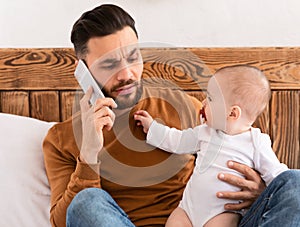 Father Talking On Phone Sitting With Baby Toddler In Bedroom