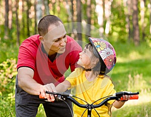 Father talking to his daughter, which teaches to ride a bike