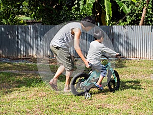 Father teach asian child boy son to ride bicycle in countryside background. Dad and young kid having sport activity and exercise