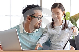 Father teaches cute girl daughter to do school homework, using laptop computer for e-learning study at home, happy family dad and