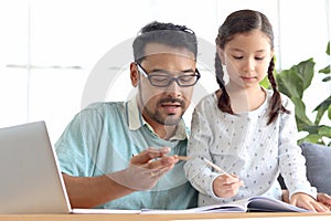 Father teaches cute girl daughter to do school homework, using laptop computer for e-learning study at home, happy family dad and