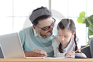 Father teaches cute girl daughter to do school homework, using laptop computer for e-learning study at home, happy family dad and