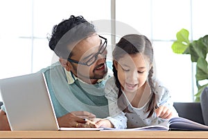 Father teaches cute girl daughter to do school homework, using laptop computer for e-learning study at home, happy family dad and