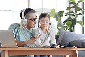 Father teaches cute girl daughter to do school homework, using laptop computer for e-learning study at home, happy family dad and