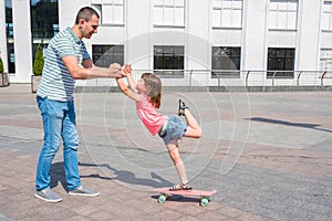 A father teaches his daughter to ride a skateboard. Family spending time together. Sunny summer day