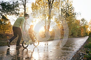 Father teaches his little child to ride bike in autumn park. Happy family moments. Time together dad and son. Candid lifestyle