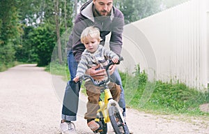 Father teaches his little child to ride bike in spring summer park, catches boy when he falls. Happy family moments. Time together