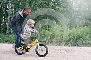 Father teaches his little child to ride bike in spring summer park. Happy family moments. Time together dad and son. Candid