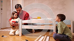 father teaches a little girl to use a tool, an electric, power screwdriver