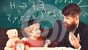 Father teaches son mathematics. Arithmetic lesson concept. Teacher in formal wear and pupil in mortarboard in classroom