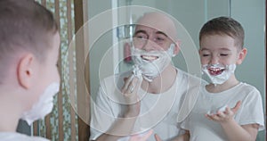 Father teaches son to shave. Little son entertains the father applies shaving cream to his face. Father and child play