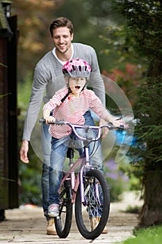 Father Teaching Daughter To Ride Bike In Garden