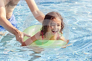 Father Teaching Daughter To Swim With Inflatable Ring In Swimming Pool On Summer Vacation