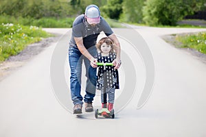 Father teaching his adorable toddler daughter to ride kick scoot