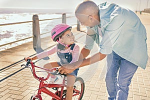 Father teaching his child to ride a bike at the beach while on a summer vacation, holiday or adventure. Happy, learning