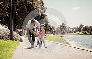 Father teaching his little daughter to ride a bike and having fun together at the park