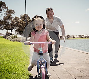 Father teaching his little daughter to ride a bike and having fun together at the park