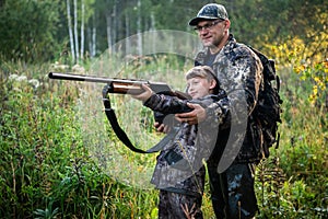 Father teaching his son about gun safety and proper use on hunting in nature.