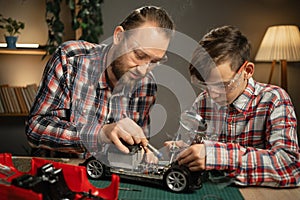 Father teaching his son for soldering and repair remote controlled car at home. Man and boy fixing broken toy.